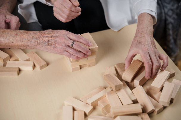 Demence terapie hravým způsobem, trénink prsty a jemné motorické dovednosti, stavět dřevěné bloky do věže, hrát Jenga. Senior žena 90 let a lékař hrát vzdělávací hru v pečovatelském domě. - Fotografie, Obrázek