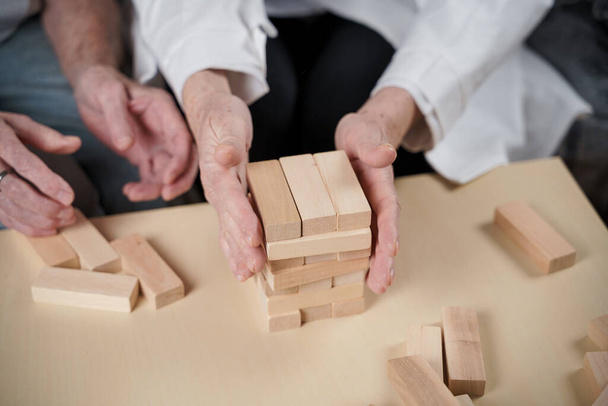 Mature doctor conducting session, therapy for senior patient in nursing home, training fine motor skills for dementia, alzheimer disease and recovery institute by folding wooden blocks, playing jenga. - Foto, Imagen