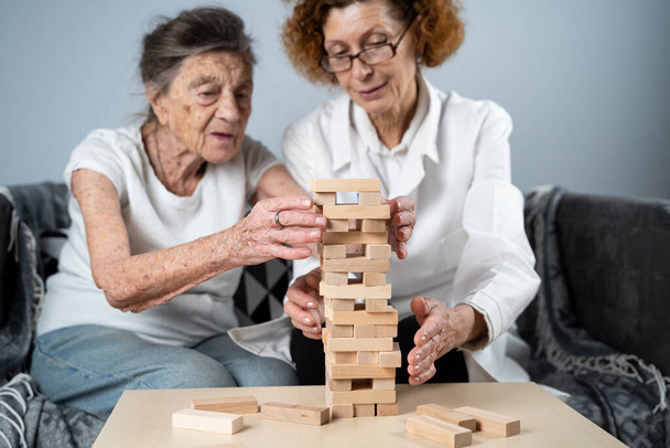 Idősebb nő, aki Jengát játszik, építsen tornyot a háztömbökből. Idős orvos fehér köpenyben, idős beteg támogatása, logika fejlesztése, finom motoros készségek, Alzheimer-kór otthon, idős magányos nő. - Fotó, kép