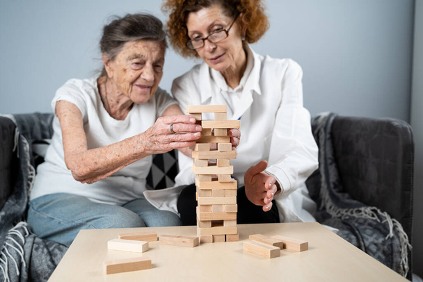 Terapia demencji w zabawny sposób, trening palców i umiejętności motoryczne, budowanie drewnianych klocków do wieży, gra Jenga. Starsza kobieta 90 lat i lekarz gra edukacyjna w domu opieki. - Zdjęcie, obraz