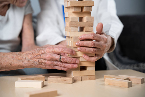 Mature doctor conducting session, therapy for senior patient in nursing home, training fine motor skills for dementia, alzheimer disease and recovery institute by folding wooden blocks, playing jenga. - Fotoğraf, Görsel