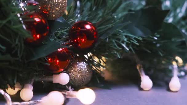 New Years or Christmas background. Close-up of the artificial fir branch decorated with red and gold Christmas balls and flashing garland light bulbs - Footage, Video