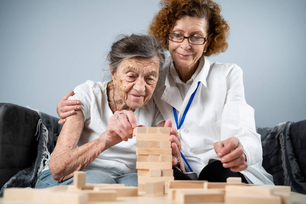 Érett orvos vezető ülés, terápia idős betegek idősek otthonában, képzés finom motoros készségek demencia, Alzheimer-kór és helyreállítási intézet hajtogatott fa blokkok, játék jenga. - Fotó, kép