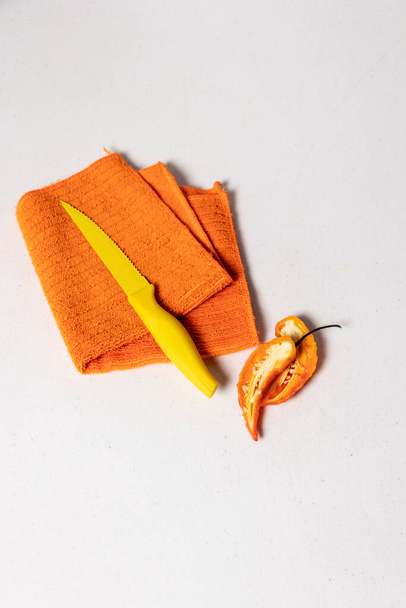 Oranje vaatdoek gevouwen met een klein geel mes naast een peper op een witte achtergrond - Foto, afbeelding
