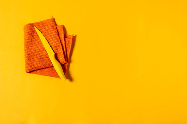 Torchon orange plié avec un petit couteau jaune sur le dessus sur un fond jaune - Photo, image