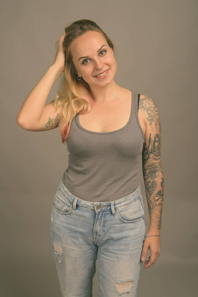 Studio shot di giovane bella donna bionda con tatuaggi a mano nel significato russo Credo e Verità su sfondo grigio - Foto, immagini