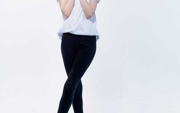 A woman in a white T-shirt and black leggings on a light background gestures with her hands cropped view - Photo, Image