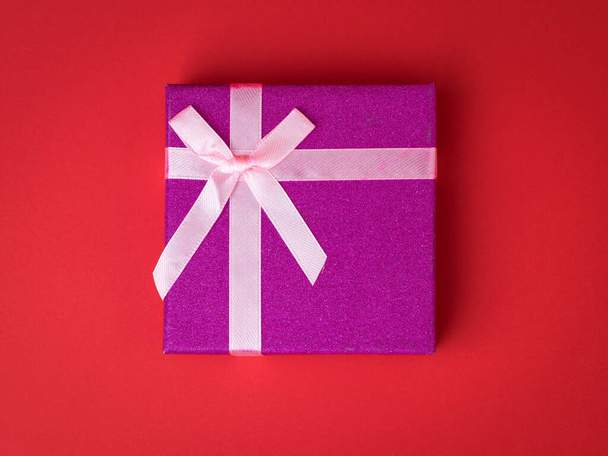 Top view of a bright box with a bow on a red background. A holiday gift. - Photo, Image