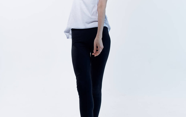 Frau drinnen auf hellem Hintergrund und schwarze Leggings in weißem T-Shirt - Foto, Bild