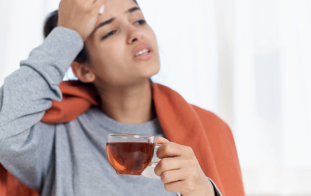 Woman with pills from hot drink indoors with orange plaid on her back - Photo, Image