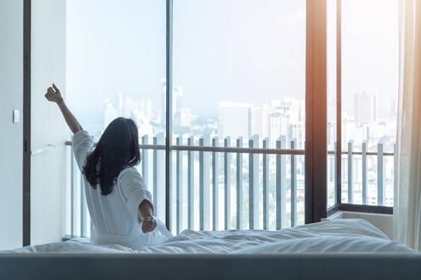 Otel odası konforu ve iyi bir uyku. Yatakta Asyalı bir kadının rahat yaşam tarzı. İyi bir sabah uyanıp, dinlenmek.  - Fotoğraf, Görsel