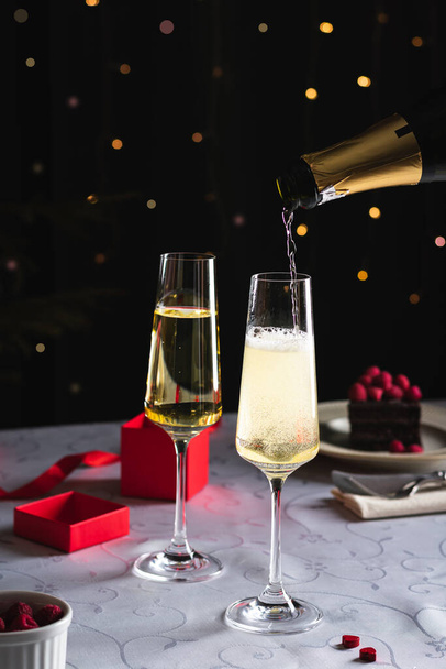 Champagne is pouring in a glass, two glasses on the table - 写真・画像