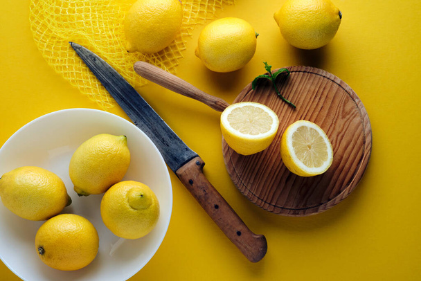 Widok z góry cytryna przecięta na pół, rustykalny nóż i świeże cytryny na żółtym tle - Zdjęcie, obraz