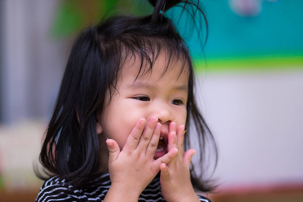 Porträt eines kleinen Mädchens, das den Bonbonkrümel, der auf ihrem Gesicht klebt, wegschmeißt. Das Mädchen isst schlampige Snacks an Händen und Mund. Ein süßes asiatisches Mädchen ist 3 Jahre alt. - Foto, Bild