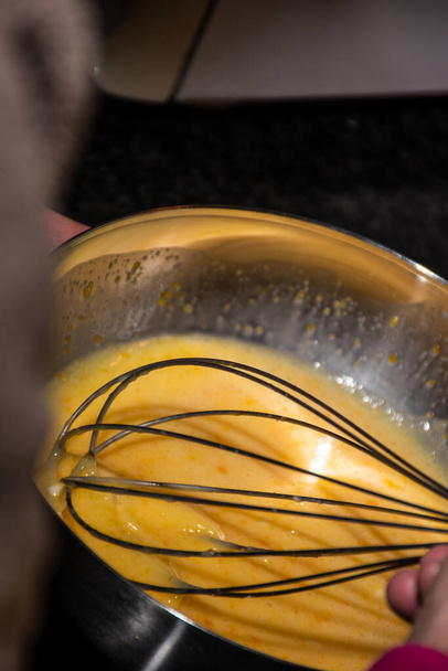 Gesloten uitzicht op een hand kloppen eieren met boter en citroen in een metalen kom. Het bereiden van een zelfgemaakt recept voor Kerstmis. De keuken klaarmaken. Gezond koken. Achtergrond met bokeh. - Foto, afbeelding