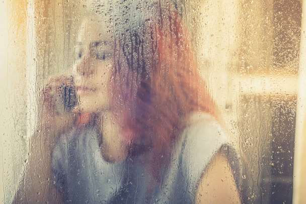 Γυναίκα με ένα μαραφέτι στα χέρια κοιτάζοντας έξω από το παράθυρο. - Φωτογραφία, εικόνα