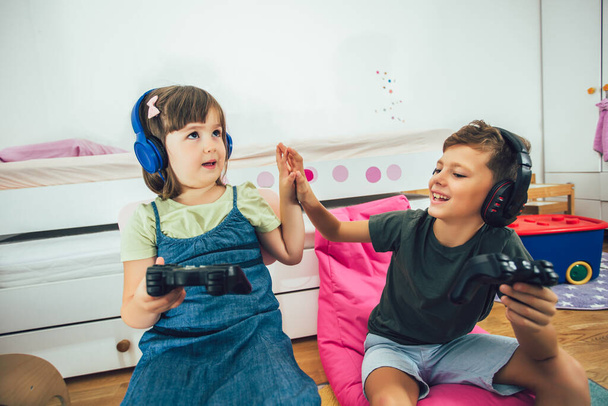 Pretty little girl and boy are playing game console and laugh at home - Foto, imagen