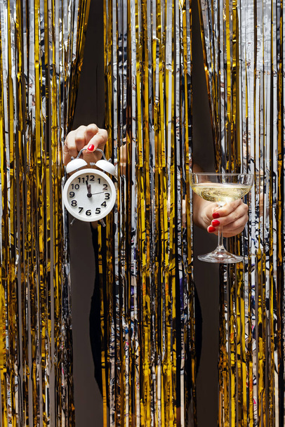Feminine hand holds clock showing almost midnight and a glass of champagne - Photo, Image