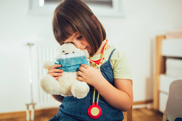 Miękki miś z ochronną maską medyczną w rękach dziecka. Dziecko bawiące się w lekarza z miękką zabawką.  - Zdjęcie, obraz