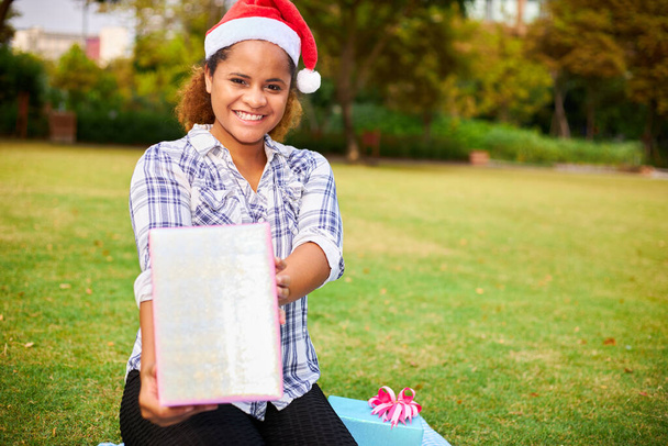 Afro-Amerikaanse vrouw draagt een Santa hoed houdt een grote geschenkdoos met een gelukkige uitdrukking. - Foto, afbeelding
