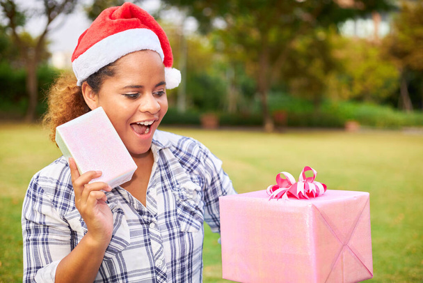 Afrikkalainen amerikkalainen nainen yllään Santa hattu omistaa iso lahja laatikko onnellinen ilme. - Valokuva, kuva