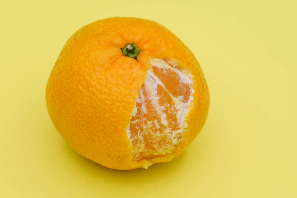 Ripe tangerine close up. Bitten off tangerine on a yellow background. Citrus fruit for immunity and health. - Photo, Image