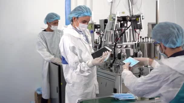 Munkavállalók egy maszkgyárban A termékek minőségének ellenőrzése modern ipari gépeken. - Felvétel, videó