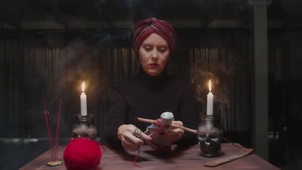 Sorcière senior diseuse de bonne aventure colle une aiguille dans une poupée vaudou dans un terrible rituel magique - Séquence, vidéo