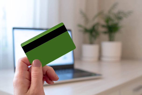 Primer plano de la mano femenina que sostiene la tarjeta de crédito en el fondo de la computadora portátil. Concepto de compras online. - Foto, Imagen