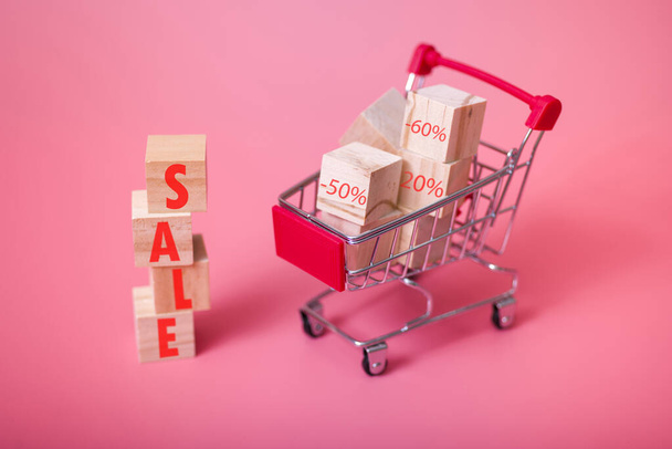 ミニチュアショッピングカートと販売レタリングと木製のブロック、孤立ピンクの背景。販売・割引の概念. - 写真・画像