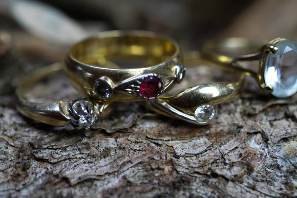 Close up of isolated old vintage golden ring with diamond and red ruby gemstone on natural tree trunk bark background - Foto, Imagem