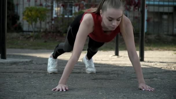 Young fit pretty woman in sportswear does exercises at sports ground outdoors - Footage, Video