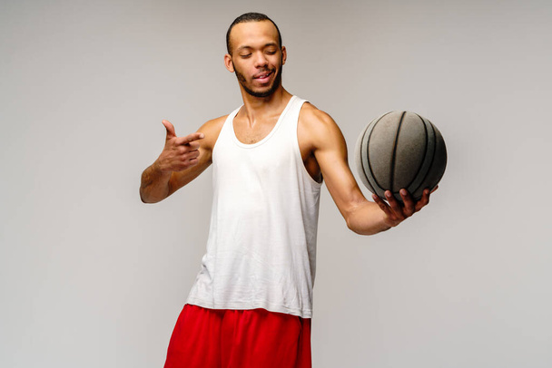 Muscular african american sportsman playing basketball over light grey background - Photo, image