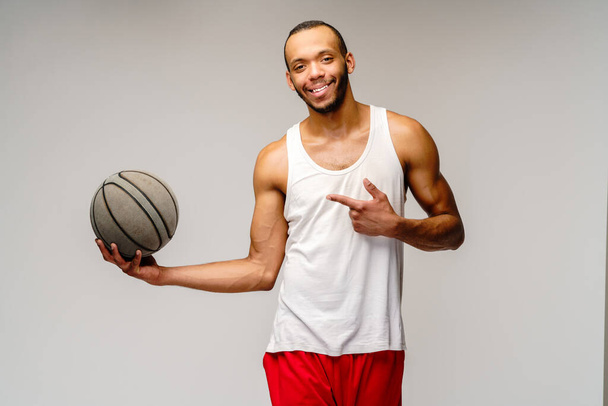 Muscular african american sportsman playing basketball over light grey background - Foto, afbeelding