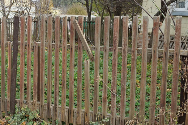 część starego brązowego ogrodzenia z rozbitą drewnianą deską na ulicy w zielonej roślinności - Zdjęcie, obraz