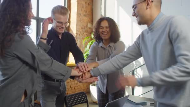 Mittlere Aufnahme fröhlicher multiethnischer Mitarbeiter, die nach erfolgreichem Geschäftsprojekt lächelnd die Hände in die Luft strecken und Spaß im Loft-Büro haben - Filmmaterial, Video