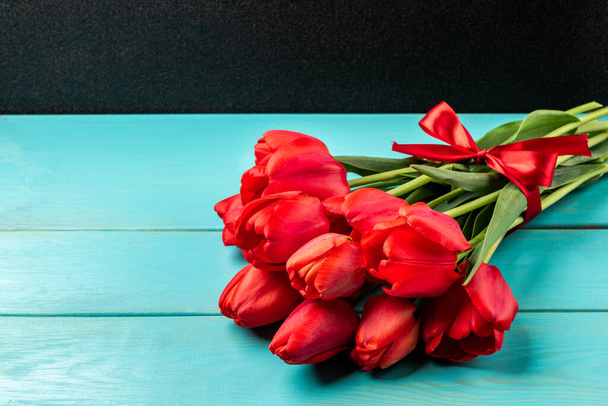 Красные тюльпаны с красной лентой на синем деревянном фоне. - Фото, изображение