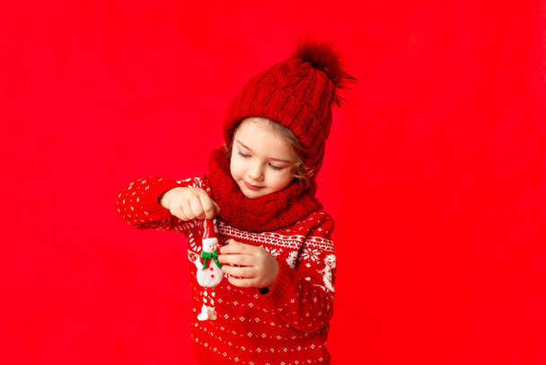pieni tyttö talvivaatteissa pitää lumiukkoa punaisella taustalla. Uuden vuoden konsepti, tilaa tekstille - Valokuva, kuva