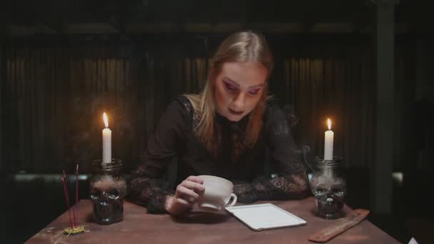 Joven bruja adivina está sosteniendo taza de café y mira la tableta a la lectura del destino - Metraje, vídeo