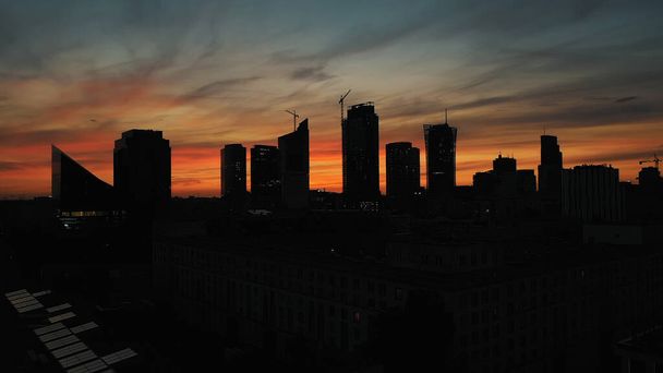 Silhouetten der Gebäude in Warschau am roten Himmel nach Sonnenuntergang. Beleuchtete Wolkenkratzer in der Stadt - Foto, Bild