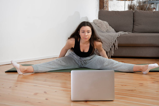 Adatta donna che fa esercizio di yoga e guarda tutorial online su laptop, formazione in salotto di casa - Foto, immagini