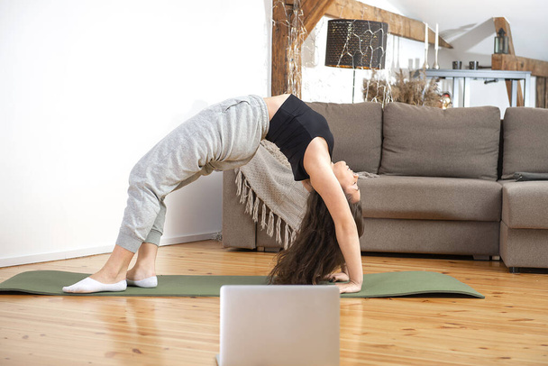 Fit femme faisant yoga exercice pont pose et regarder des tutoriels en ligne sur ordinateur portable, formation à la maison  - Photo, image