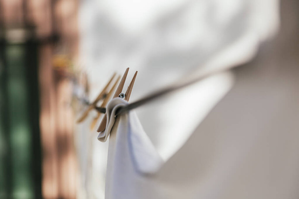 White clothes hanging on a clothesline with wooden clothespins. The clamp is in focus, the rest is out of focus. A window with black bars can be seen in the background. - Foto, immagini