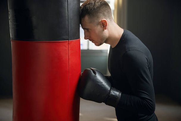Tired boxer after training. A boxer stands by a punching bag. Workout in the gym. Sweaty athlete in the gym. 4k - Photo, Image