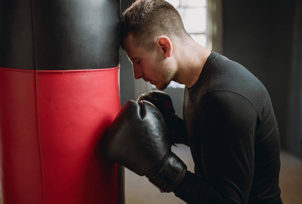 Boxer fatigué après l'entraînement. Un boxeur se tient près d'un sac de boxe. Entraînement dans la salle de gym. Athlète en sueur dans la salle de gym. 4k - Photo, image