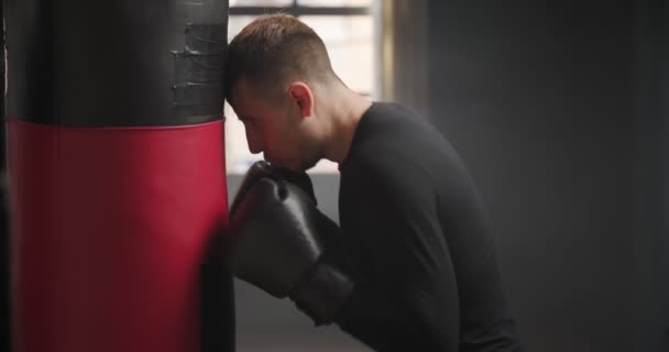 Boxer fatigué après l'entraînement. Un boxeur se tient près d'un sac de boxe. Entraînement dans la salle de gym. Athlète en sueur dans la salle de gym. 4k - Séquence, vidéo