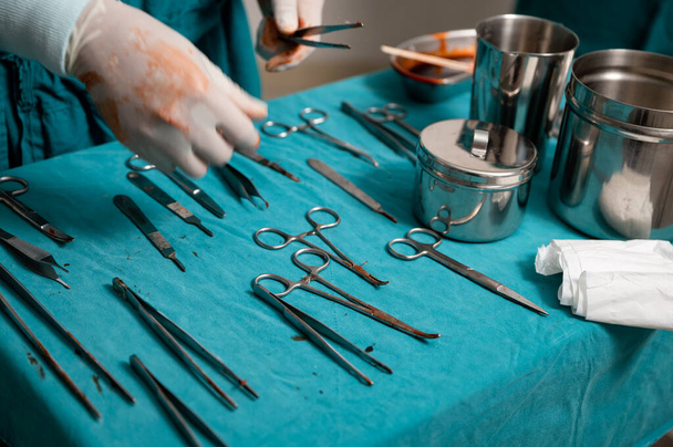 Ręka chirurga nosić rękawice medyczne wybierając instrumenty chirurgiczne na stole w sali operacyjnej - Zdjęcie, obraz