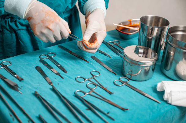 La mano del cirujano usa guantes médicos eligiendo instrumentos quirúrgicos en una mesa en el quirófano - Foto, imagen