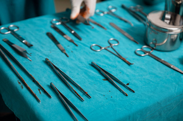 Рука хірурга носить медичні рукавички, вибираючи хірургічні інструменти на столі в операційній
 - Фото, зображення