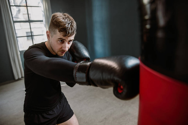 Egy fiatal atlétikai férfi bokszzsákot üt. Boxer ütéseket gyakorol a ringben. A sportoló bokszzsákkal üt.. - Fotó, kép